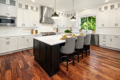 White kitchen with a black island and dark stained wood floors.