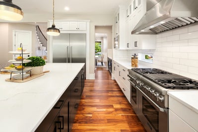 Island on the left with white stone countertops and black cabinets, on the right is white cabinets with black accents and a gas stove.
