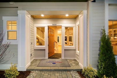 Exterior view of a light wood front door with windows on each side and white trim.