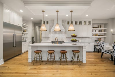 Kitchen with industrial size fridge, three lights above over sized island, white cabinets and white stone countertops.