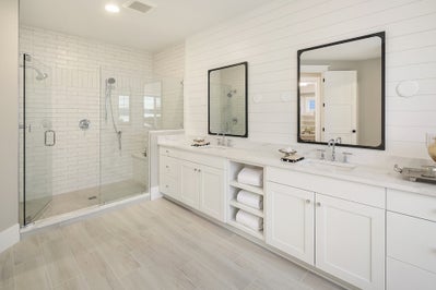 Double sink white vanity with white countertops next to a large tiled walk in shower.