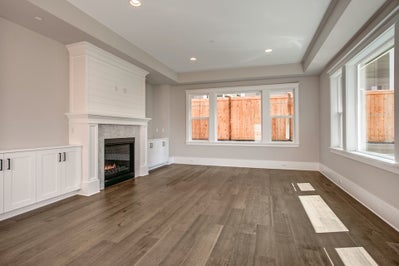 Living room with tray ceiling, wood floors and two large windows.