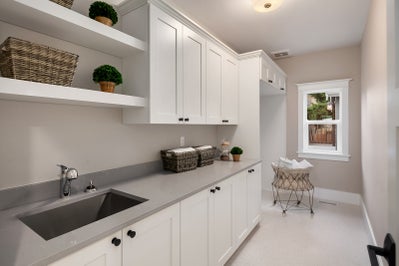 Laundry room with sink, folding counter, white cabinets and a window.