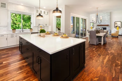 Kitchen island with white stone countertop, dark cabinets and view of living spaces