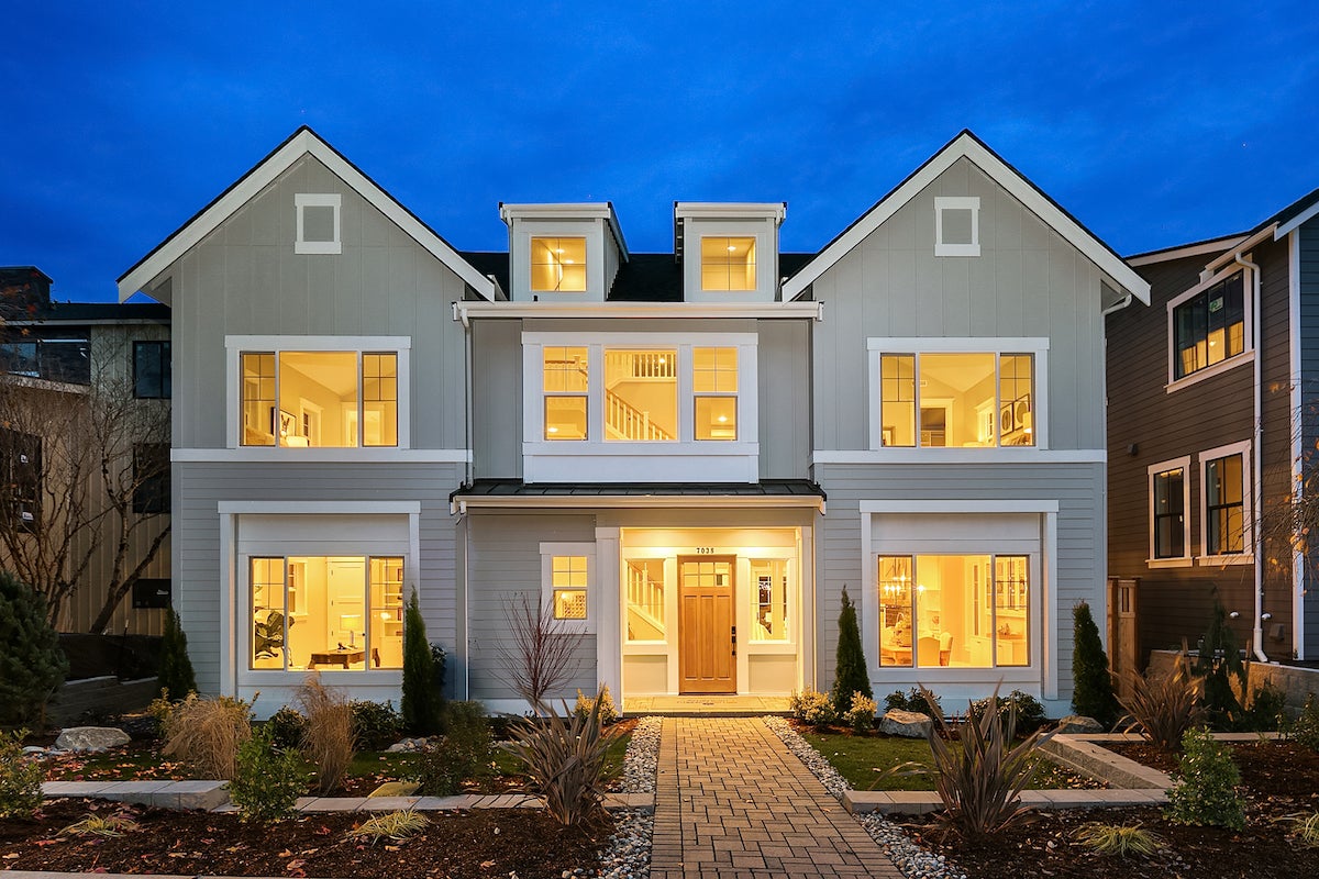 Two story light gray home with white trim and lights on