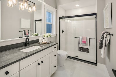 Bathroom with tiled walk in shower and a white vanity with gray stone countertop and black matte finishes