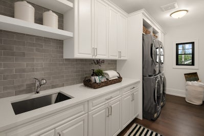 Laundry room with sink, folding counter, white cabinets and space for two sets of stackable washer and dryers.