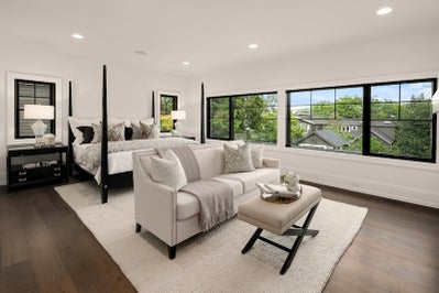 Large master bedroom features a loveseat couch in front of the bed and windows span across the far wall.