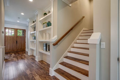 White staircase with dark wood accents sits next to built in shelving.