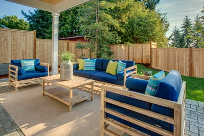 Covered patio with sitting space overlooking fenced and landscaped yard.