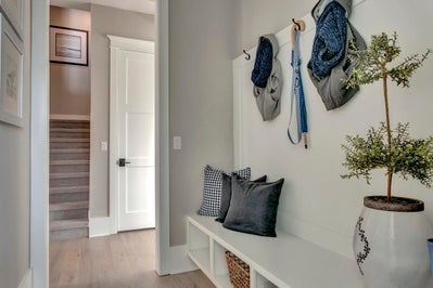 Mudroom with built in coatrack and bench leads to hallway with staircase.
