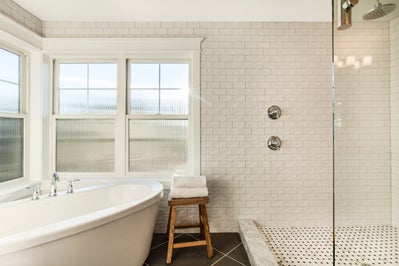 Large walk in shower is open to the bathroom and sits next to soaking tub, walls are a white tile.