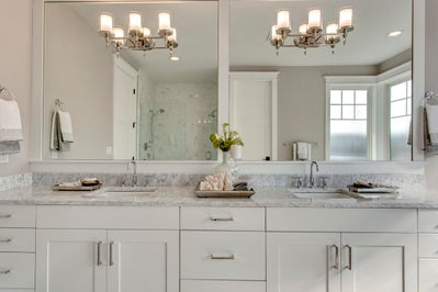 Vanity with white cabinets, gray stone countertops, doube sinks and a large mirror.