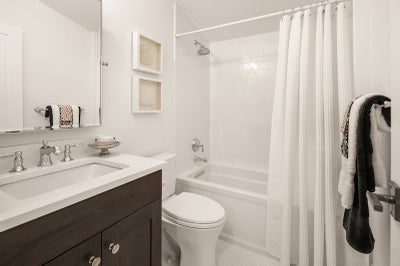 Private bathroom with tub and shower, wood vanity with white stone countertop.