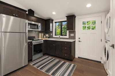 Private kitchen with wood cabinets, stone white countertops, wood flooring and stacked washer and dryer.