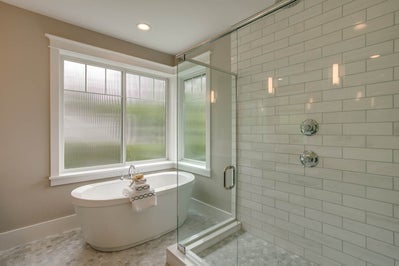 Glass incased shower with tile surround sits next to a soaking tub.